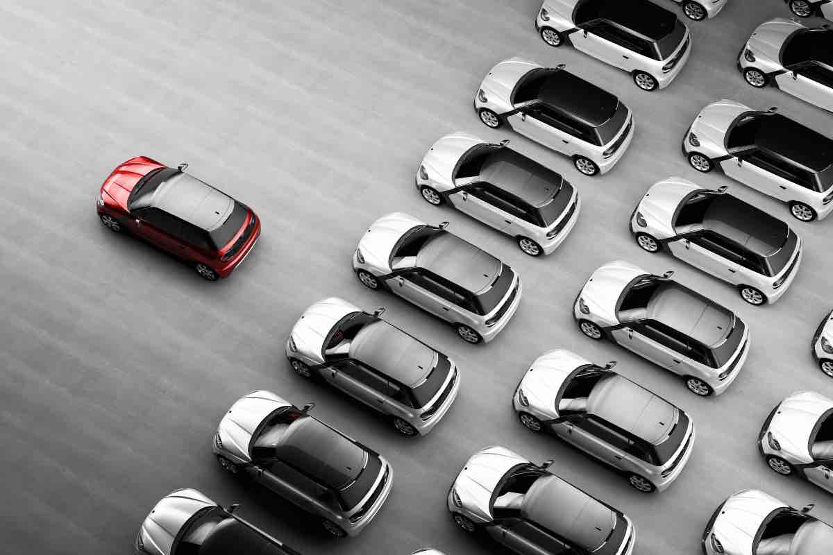 Un'auto rossa davanti a tante auto tutte uguali