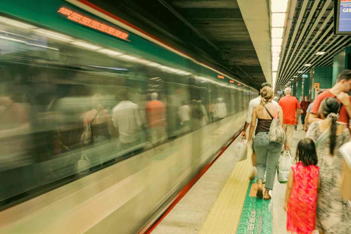 Tante persone vicino ad una metro che passa a sinistra