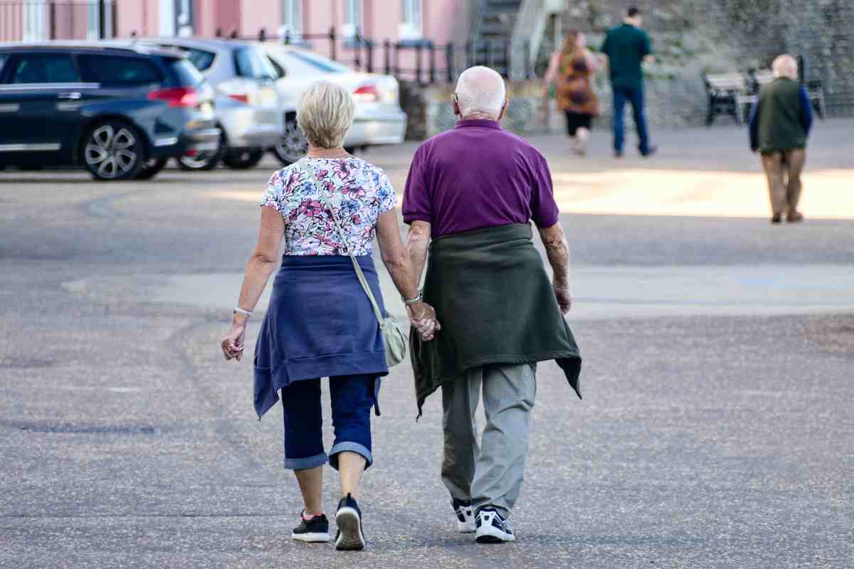 Uomo e donna camminano mano nella mano, ripresi di spalle