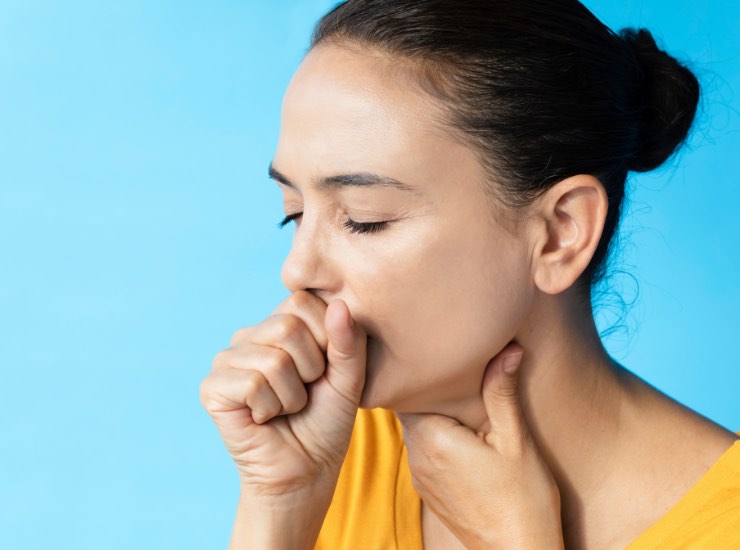 Una ragazza tossisce tenendosi la gola